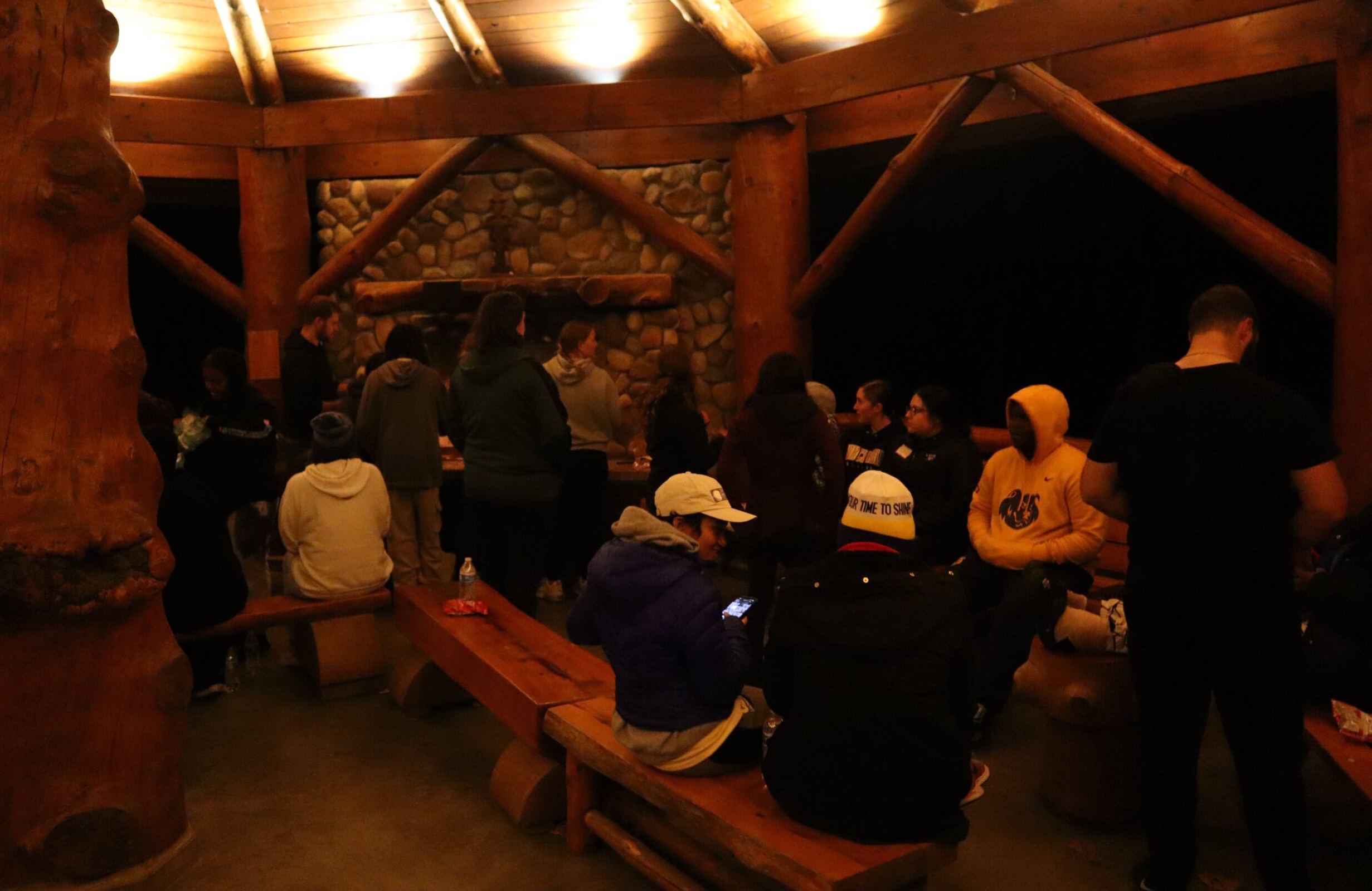 Group of students in a dimly lit cabin sitting on wooden benches