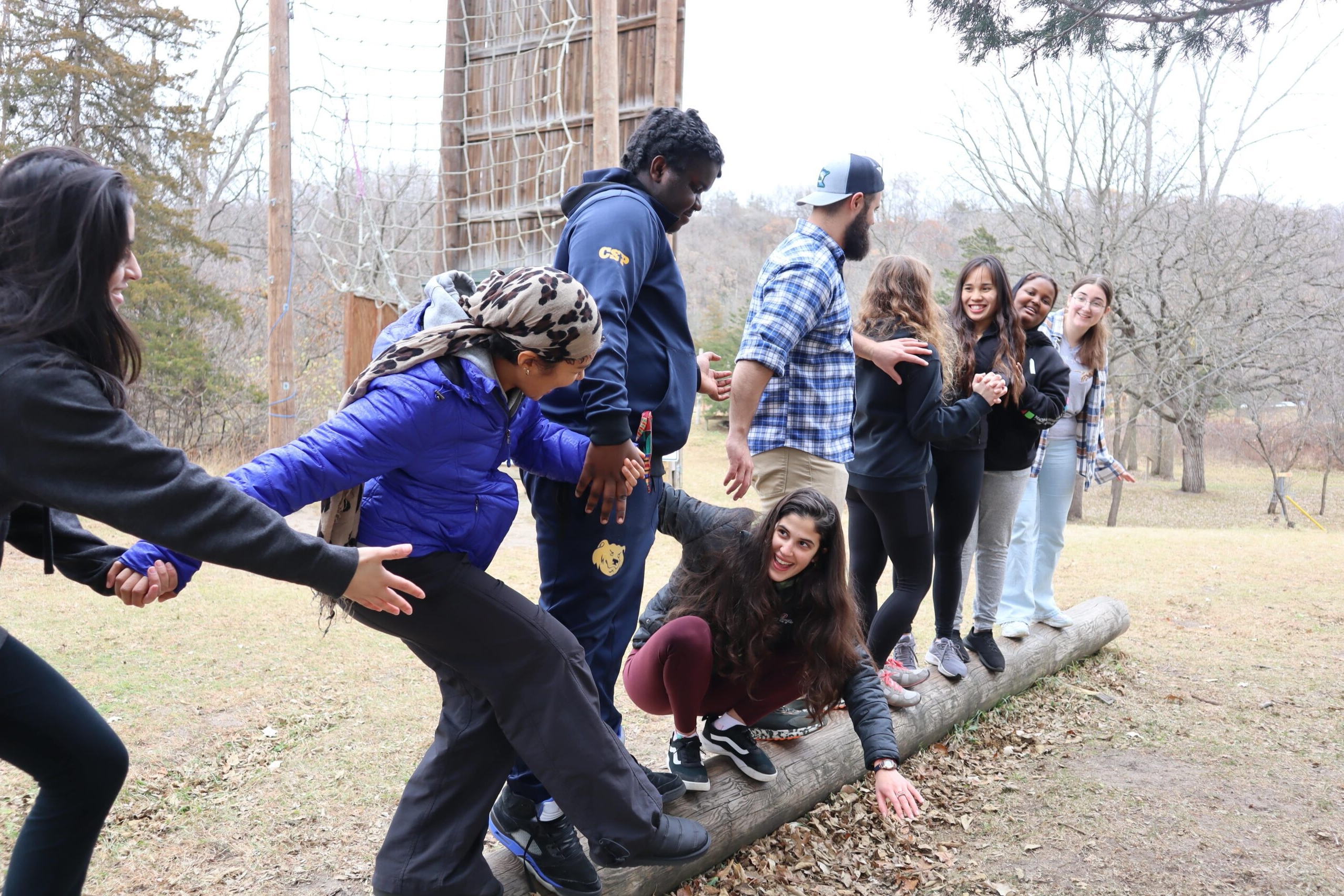 Group of students partaking in a team building activity. All standing on a log holding hands.
