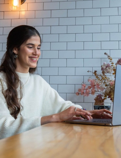 Student smiling and looking at a laptop while sitting in a coffee shop.