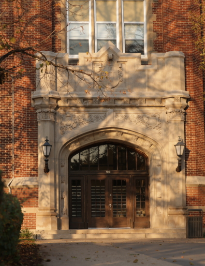 Brown and gray stone building with an ornate entrance and a light on each side of the doorway.