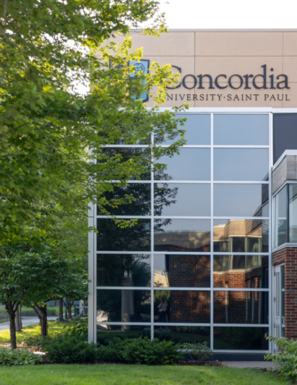 Tan Concordia building with trees in front of it in summertime.