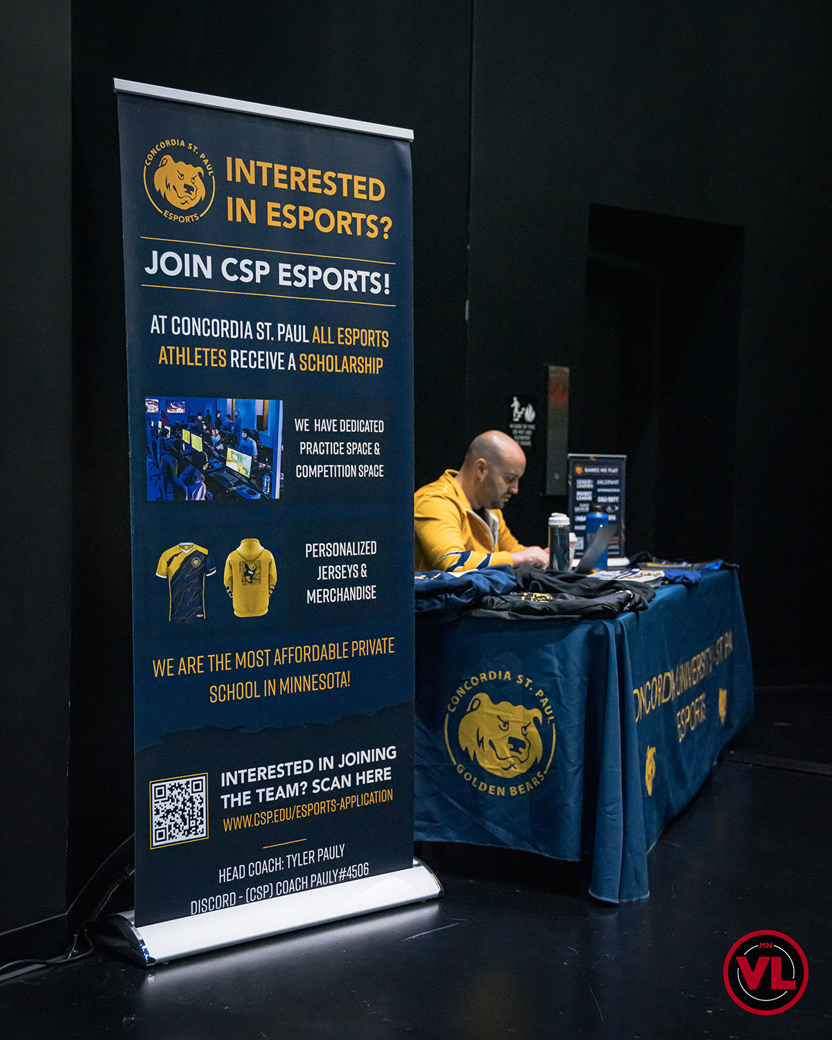 Esports coach sitting at an information table booth.